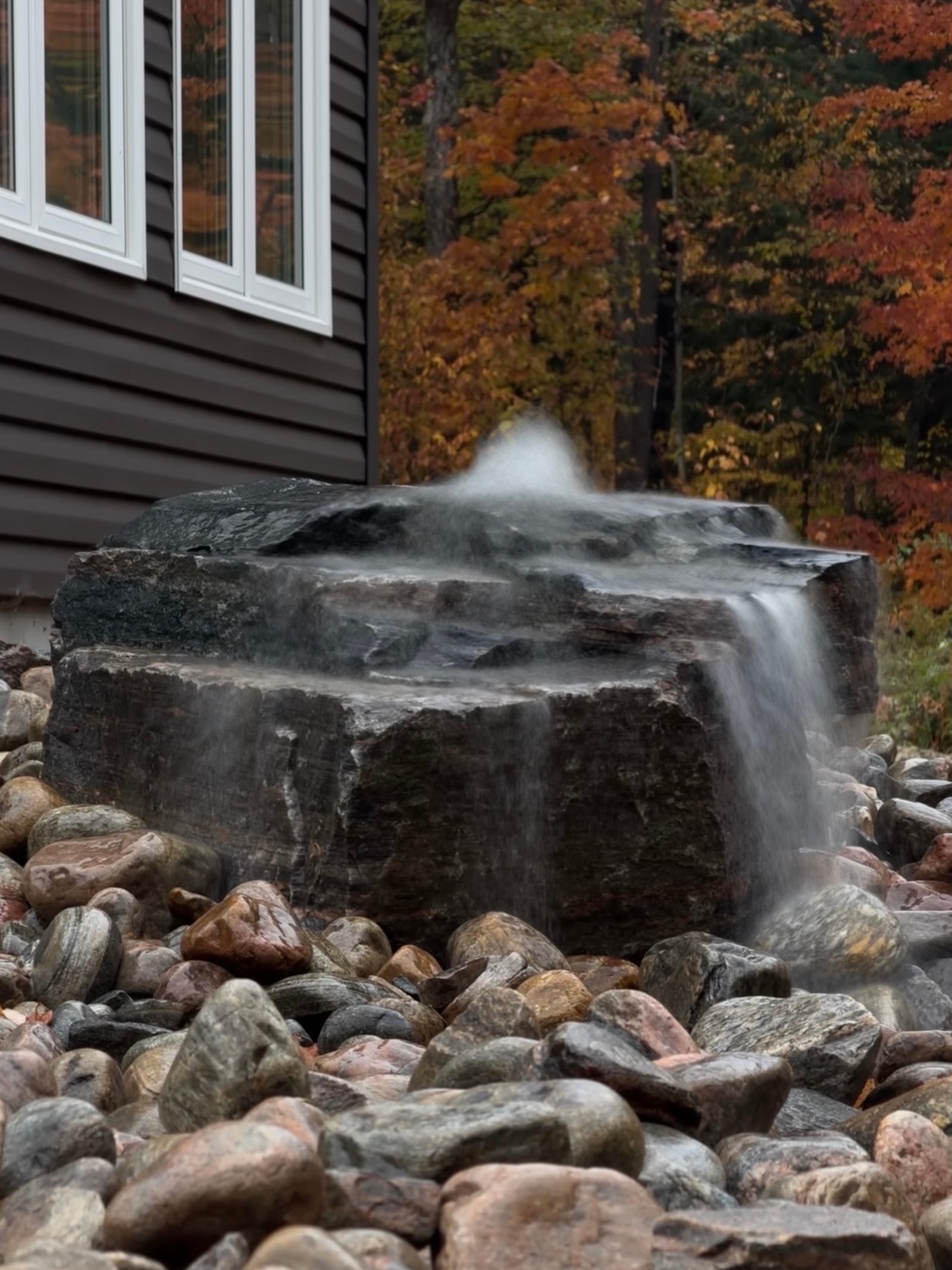 Long exposure of water flowing over a granite boulder in a pondless water feature, fall colour behind, Huntsville